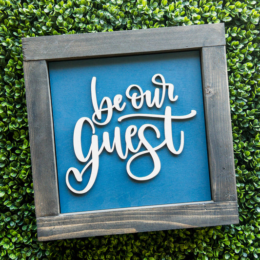 Interchangeable porch decor tile with Be Our Guest white script on blue in a grey frame | Millie & Co.