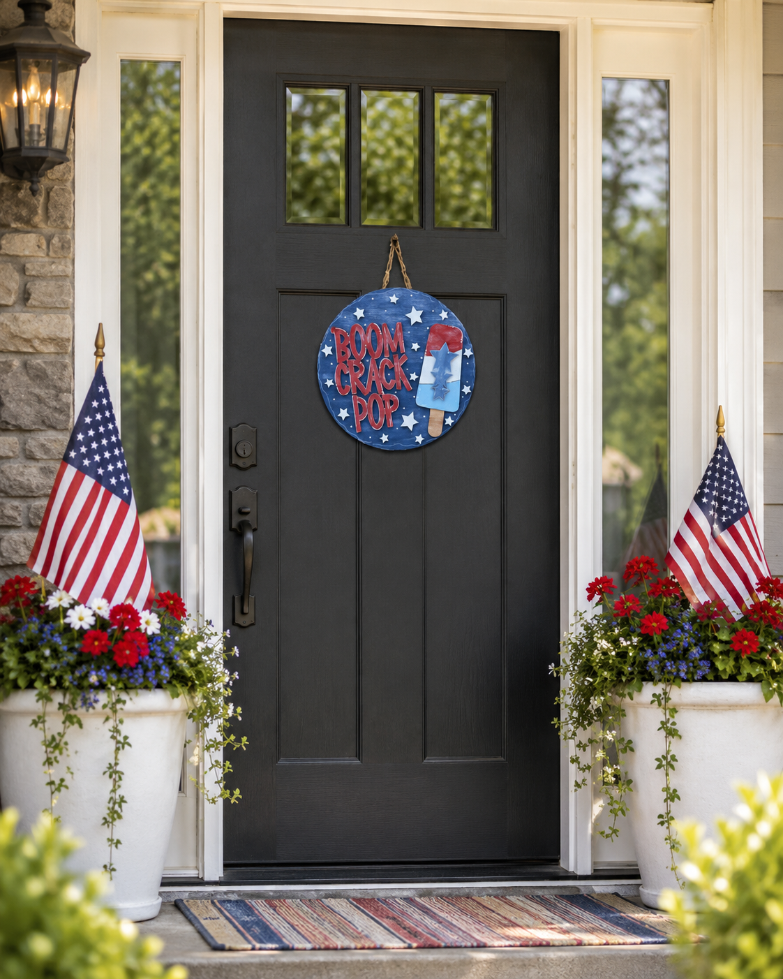 Boom Crack Pop door round hanging on a black front door between American flags and red, white, and blue planters
