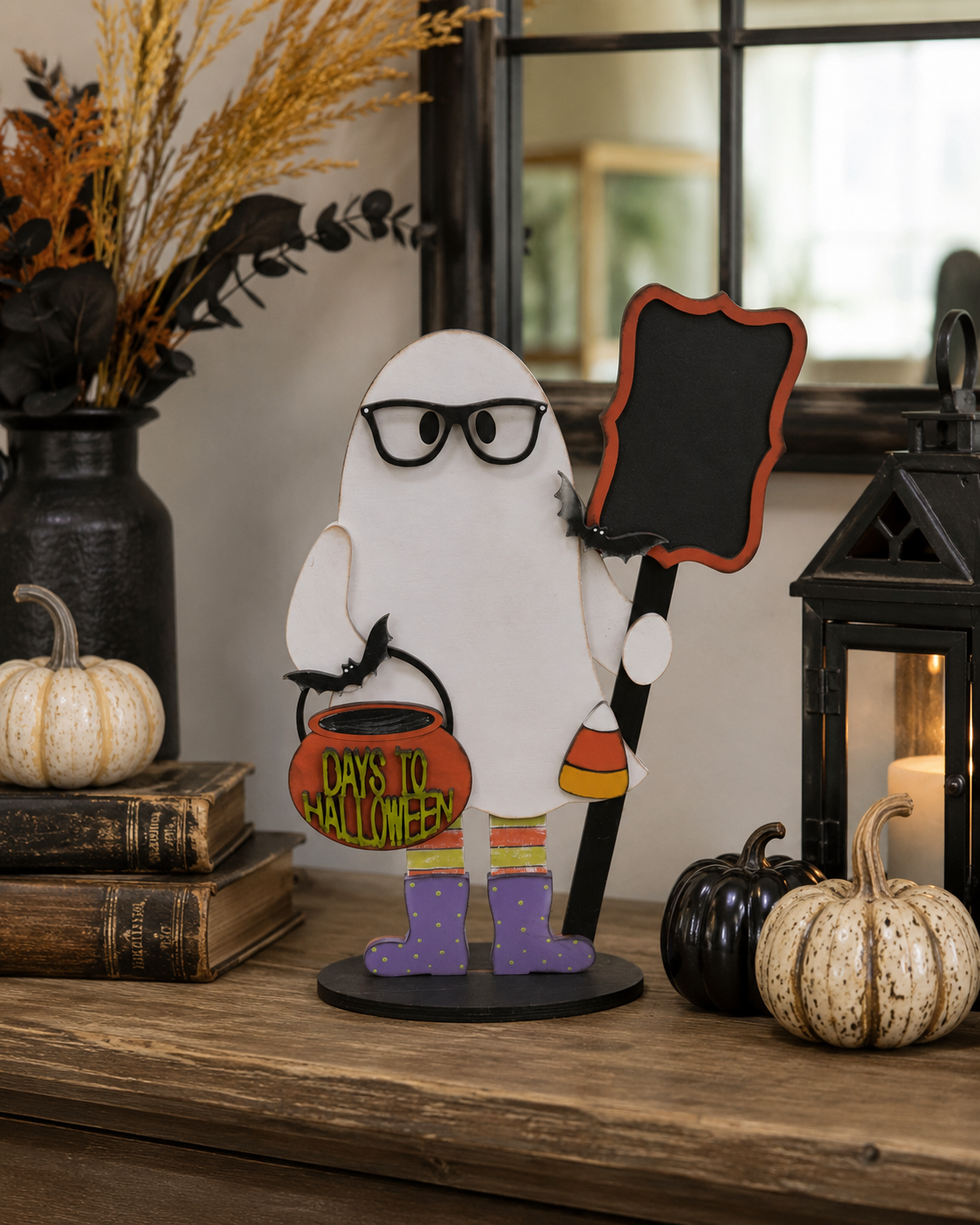 Hand-painted ghost stander in glasses holding a bat bucket and chalkboard countdown sign, displayed on a console table with pumpkins and a lantern