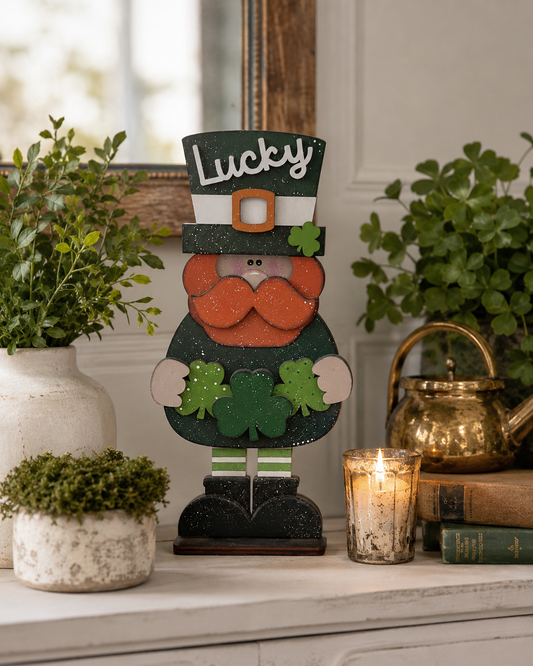 Hand-painted Lucky Leprechaun stander with shamrock hat and beard displayed on a mantel between potted greenery and a candle