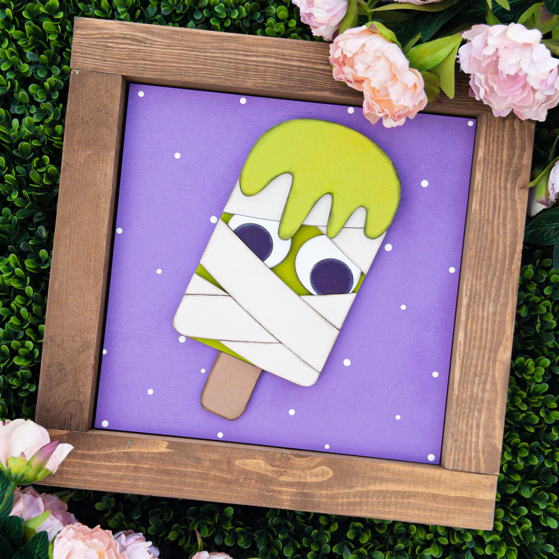 Seasonal porch decor tile of a lime green mummy popsicle with bandage wraps on a purple polka-dot background — Millie & Co.