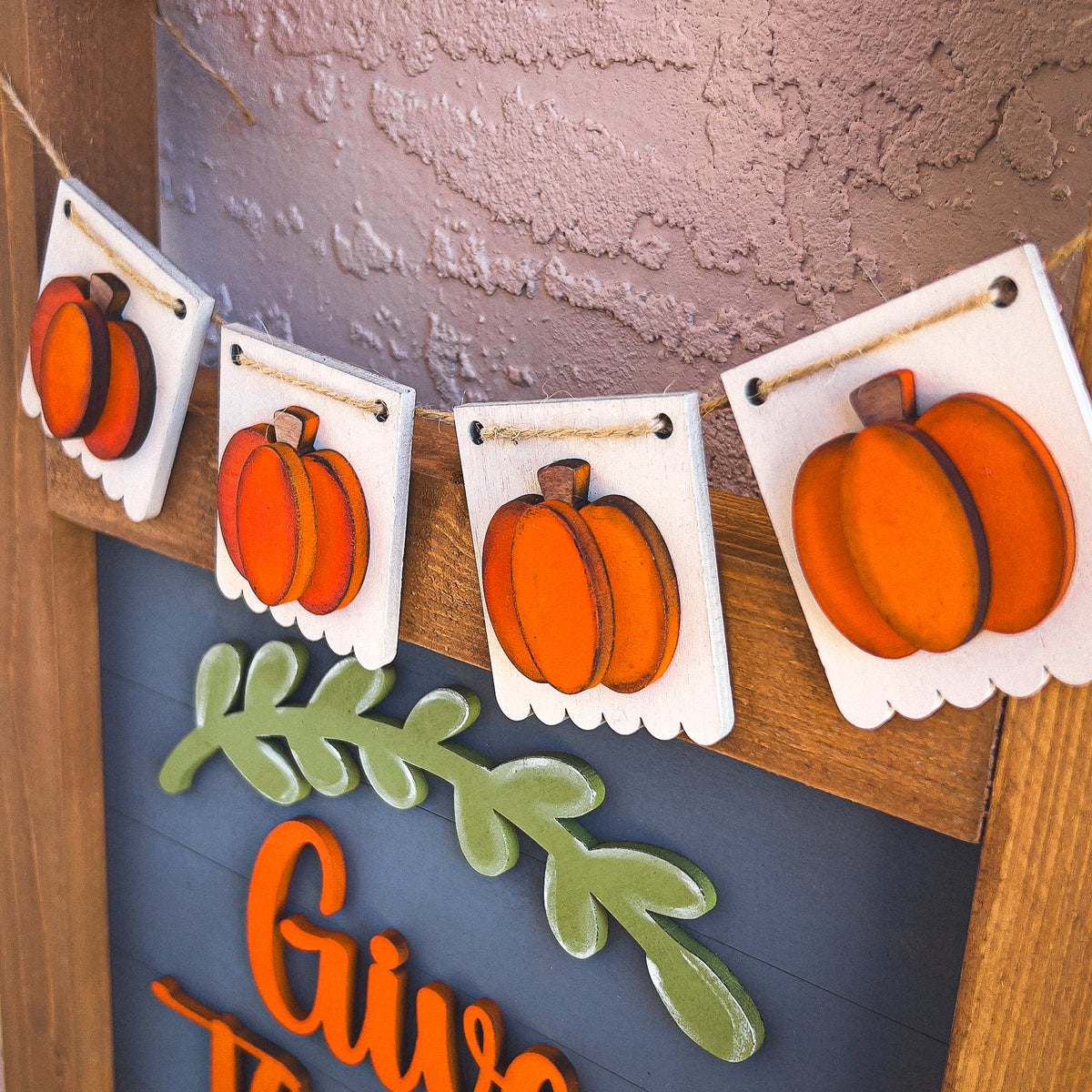 Pumpkin fall porch decor ladder wrap with four hand-painted orange pumpkin banners on jute twine across an interchangeable porch ladder | Millie & Co.